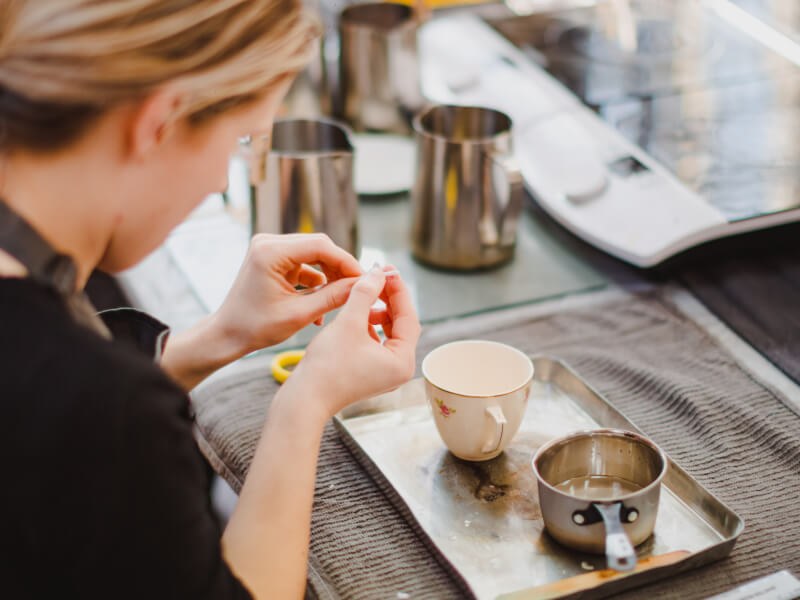 Hands preparing a candle wick to be placed into a DIY teacup candle. A tiny saucepan holds the candle wax.